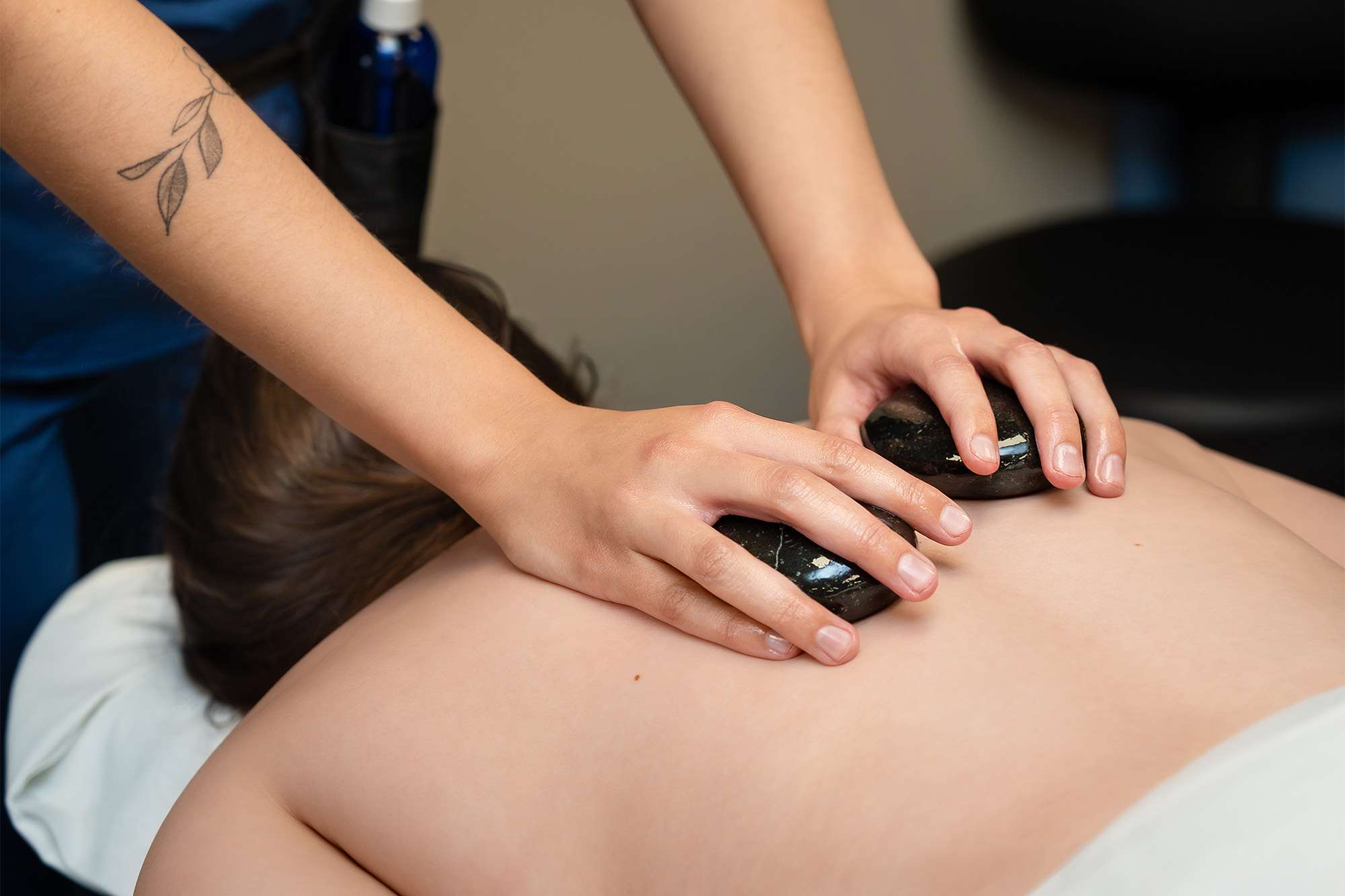 A massage therapist holds a smooth hot rock in each hand to massage the back of a patient.