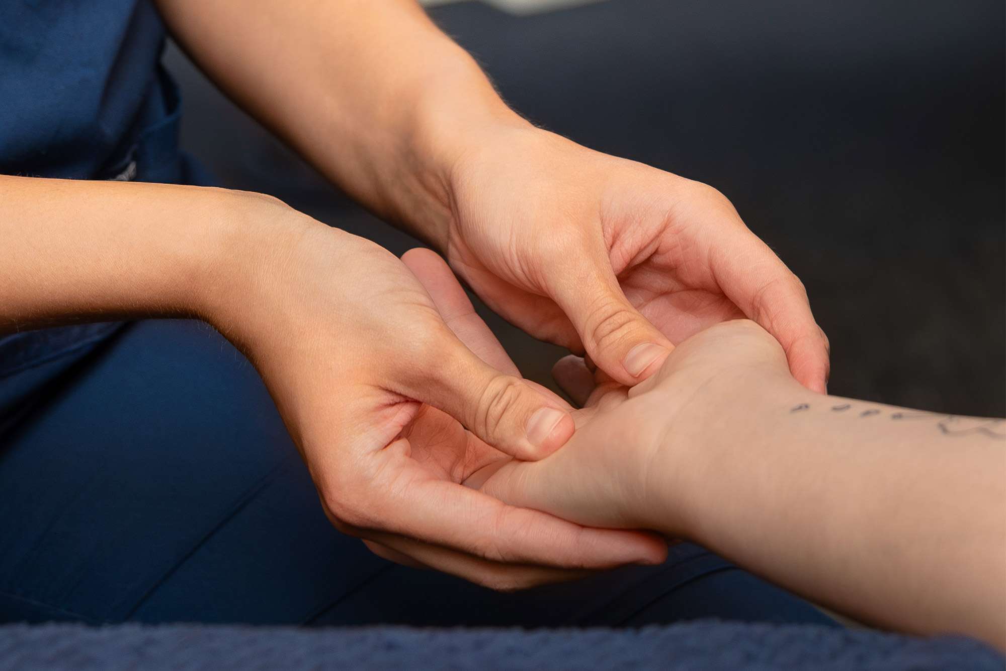 A close up view of a massage therapist using both hands to massage the palm of a patient's hand.
