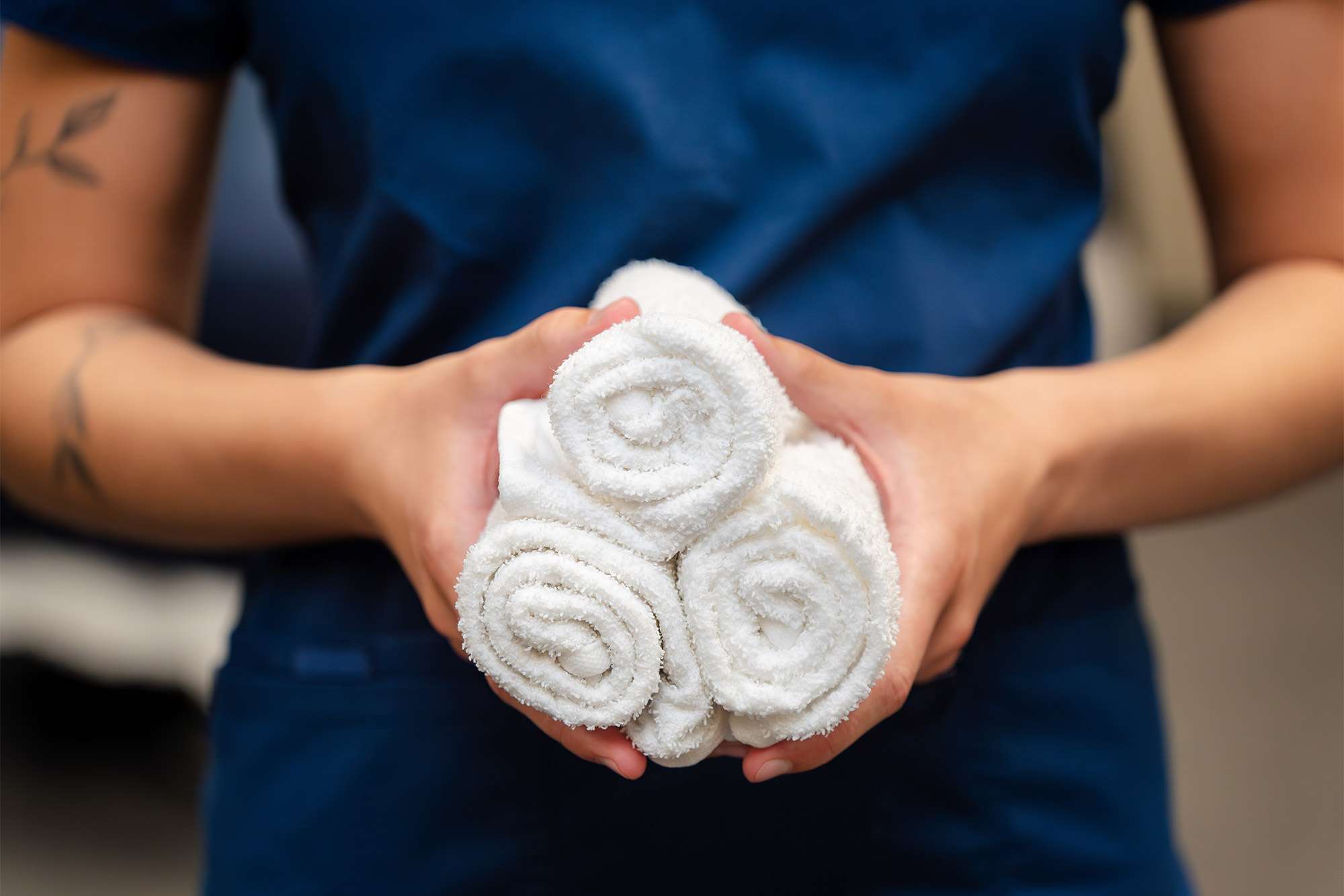 A close up view of a massage therapist holding three rolled up white towels in her hands.
