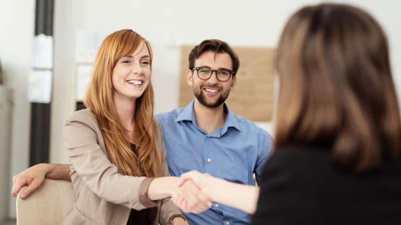 A wife and husband sit together with a financial advisor and shake her hand