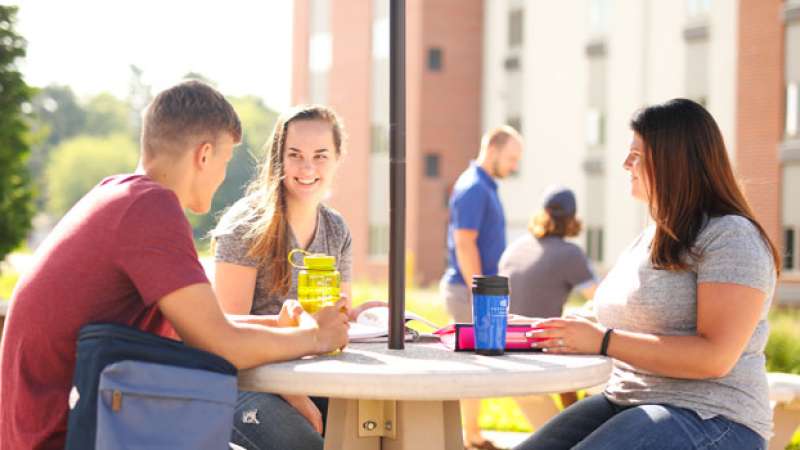 Three students are sitting together working on homework and having a conversation with each other