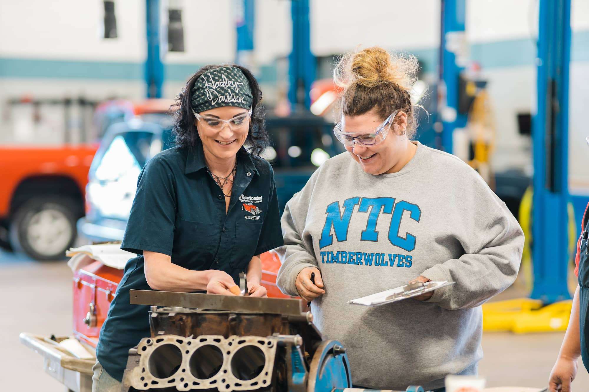 An instructor and automotive student collaborating to take notes on the status of a 6 cylinder engine block.