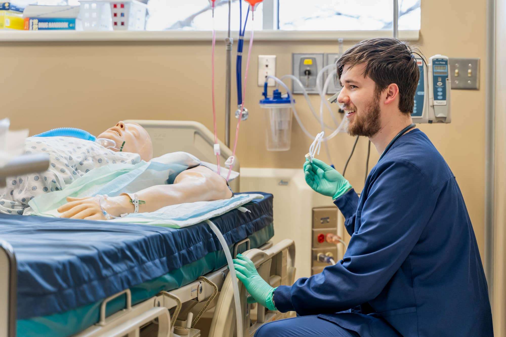A student smiles while kneeling near the side of a patient's bed and talking with his team.