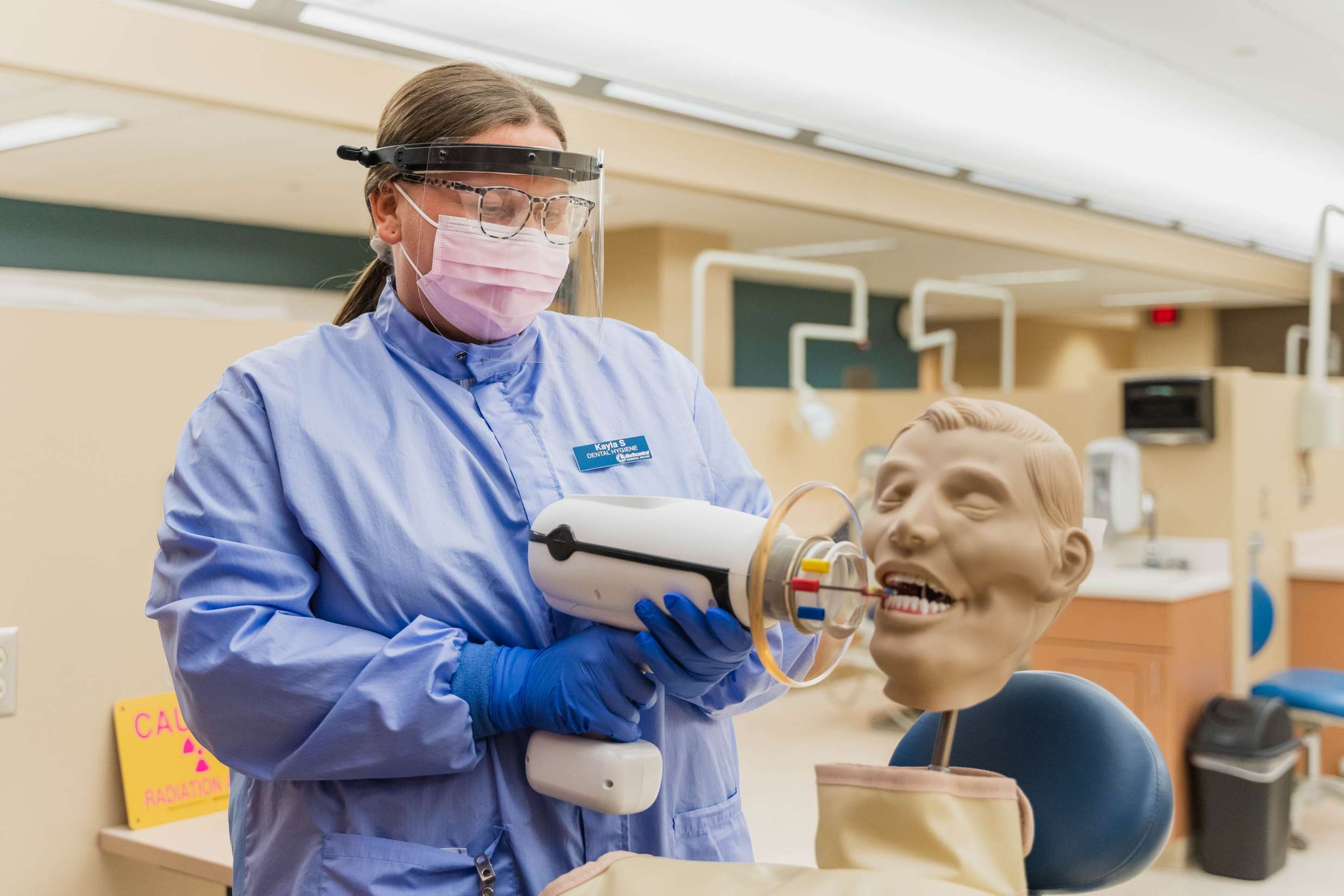 A dental hygienist performs procedures on a mannequin head positioned upright in a procedure room chair.