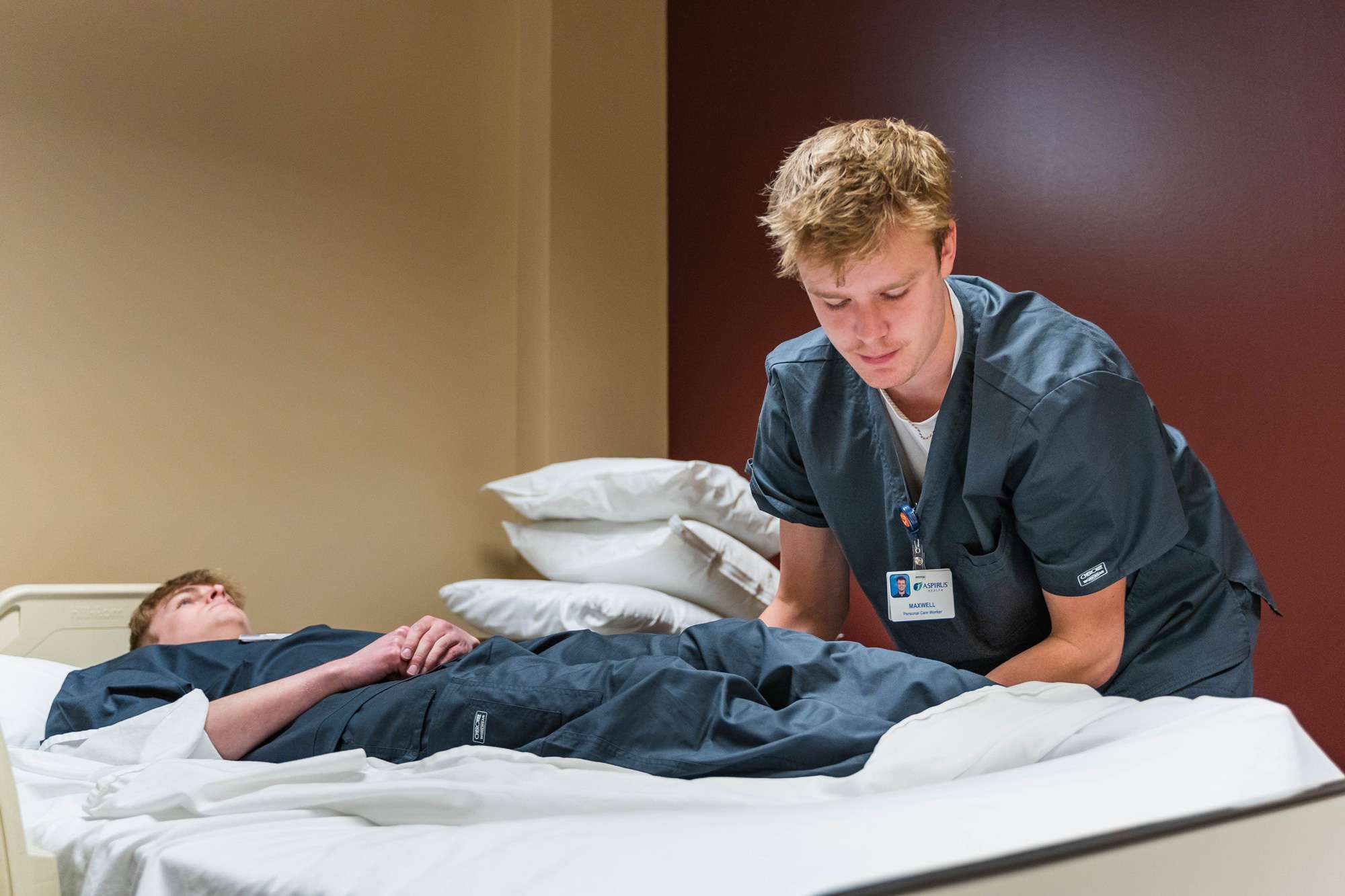 A Nursing Assistant is repositioning a patient on a hospital bed.