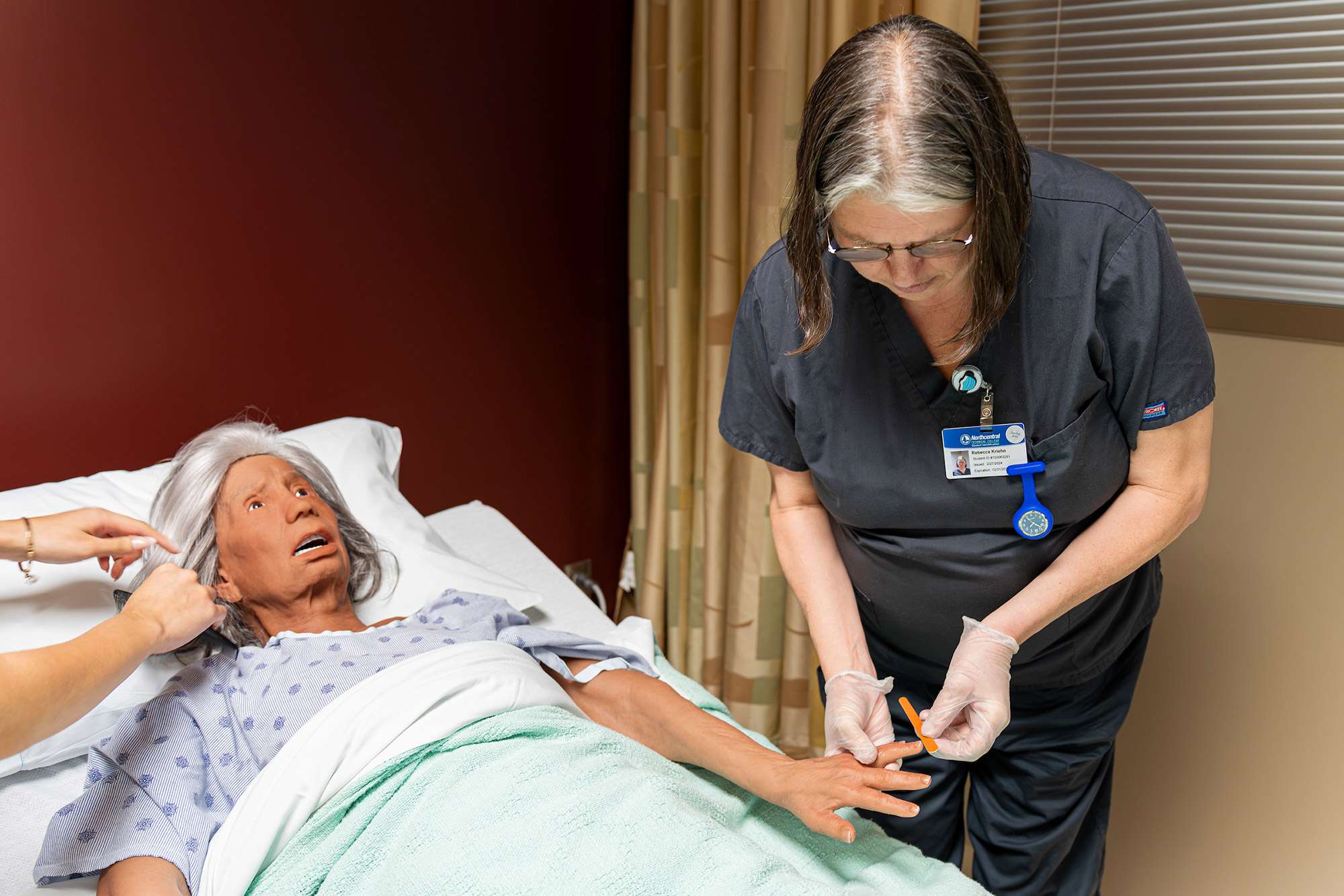 A certified nursing assistant uses a naile filer on the hand of a mannequin