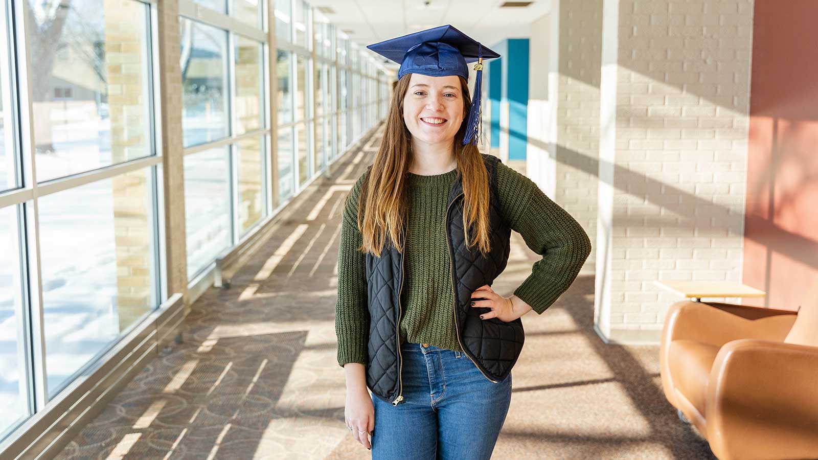 Samantha posing while wearing an NTC graduation cap in the hallway.
