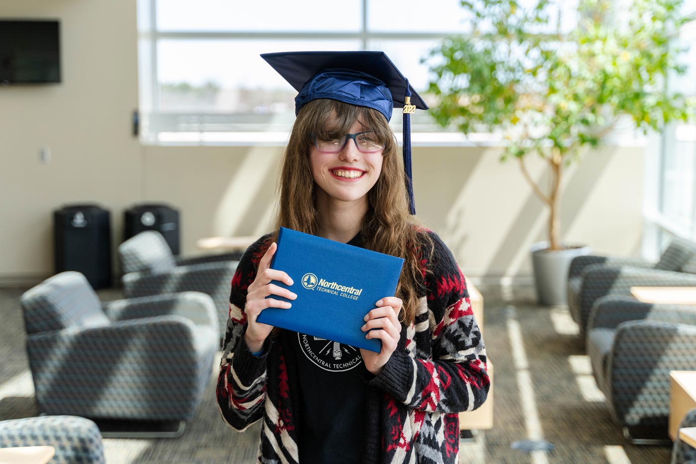 Carly posing while wearing an NTC graduation cap and holding her diploma.
