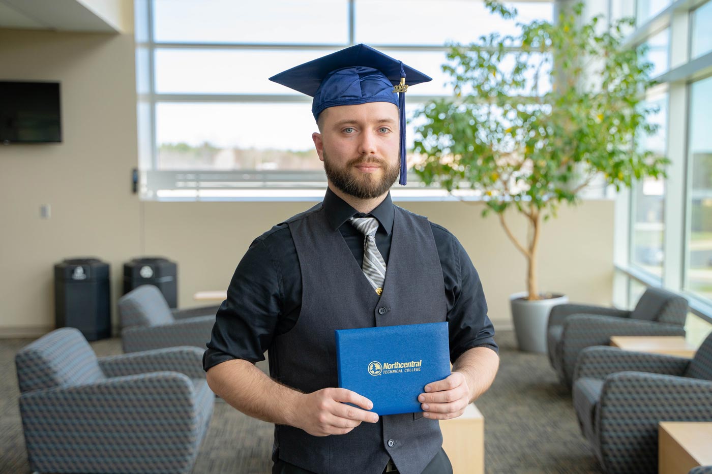 William posing while wearing an NTC graduation cap and holding his diploma.