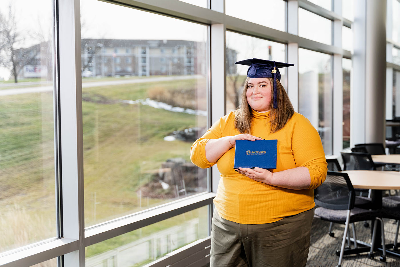 Daryl posing while wearing an NTC graduation cap and holding her diploma.