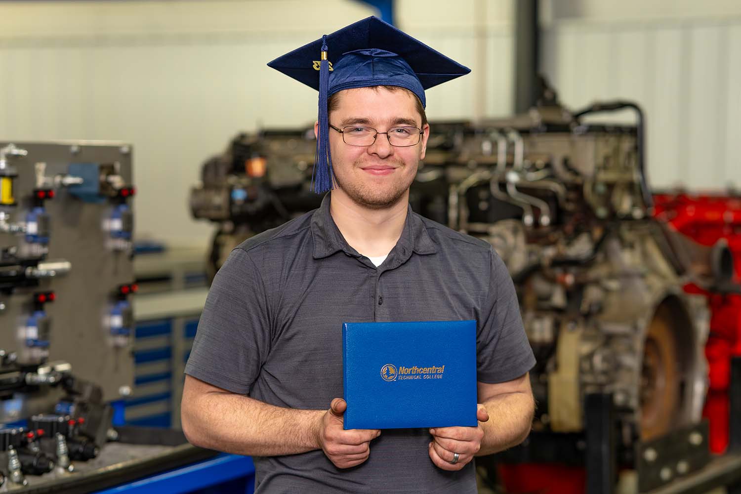Jonathan posing while wearing an NTC graduation cap and holding his diploma.