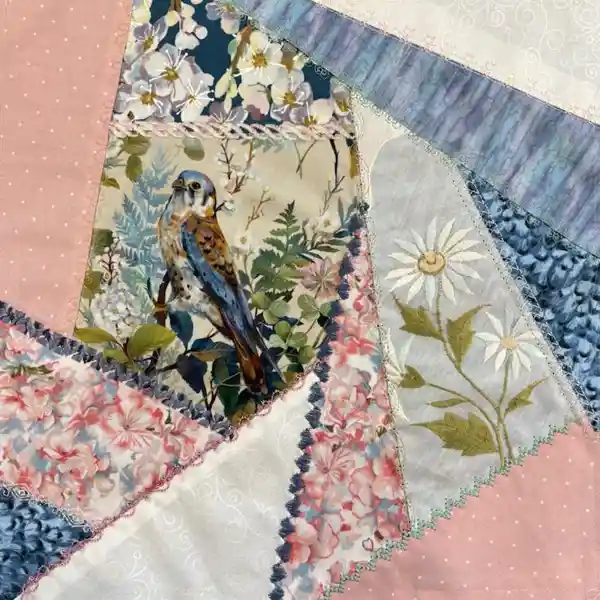 Quilted fabric featuring a bird among foliage, white daisies, pink polka dots, and blue patterns, all sewn together with decorative edges.