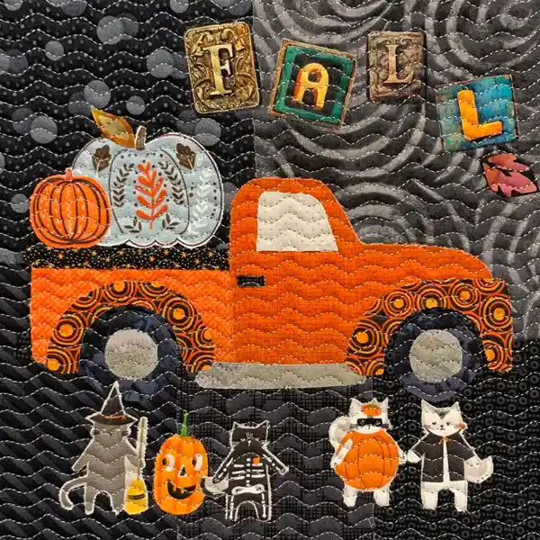 A quilted scene features an orange truck with pumpkins in the bed, and the word 'FALL' above. Below, several cats wear Halloween costumes.