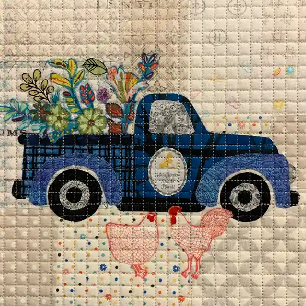 Quilted fabric block featuring a blue plaid pickup truck with colorful flowers in its bed and two pink outline-stitched chickens.