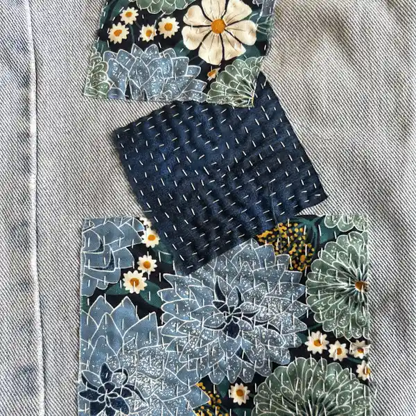 Three fabric patches layered on light blue denim. Two are patterned with blue and white flowers; one is dark blue with white visible stitching.