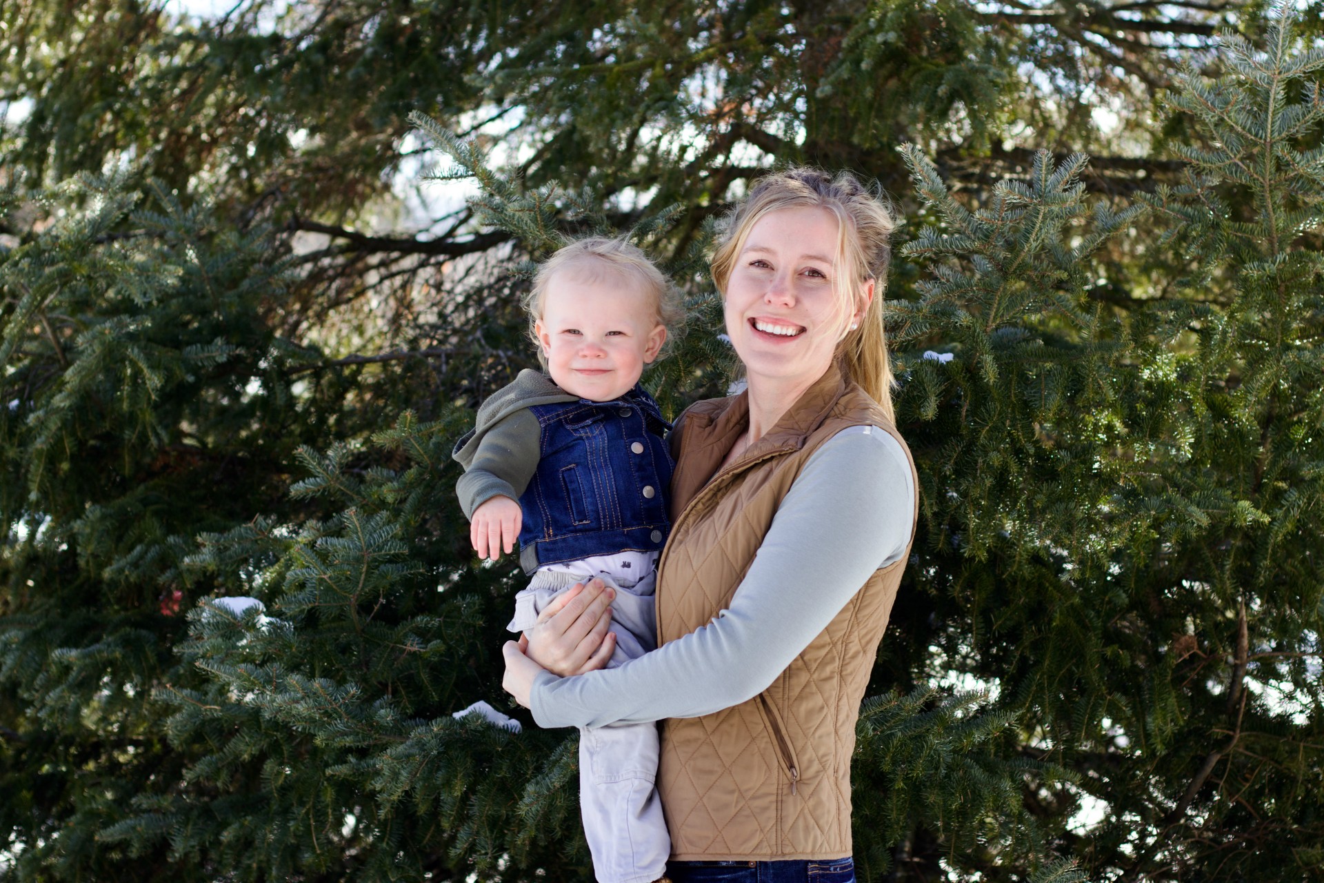 Abigail Schulz holding a baby while standing in front of a coniferous tree.
