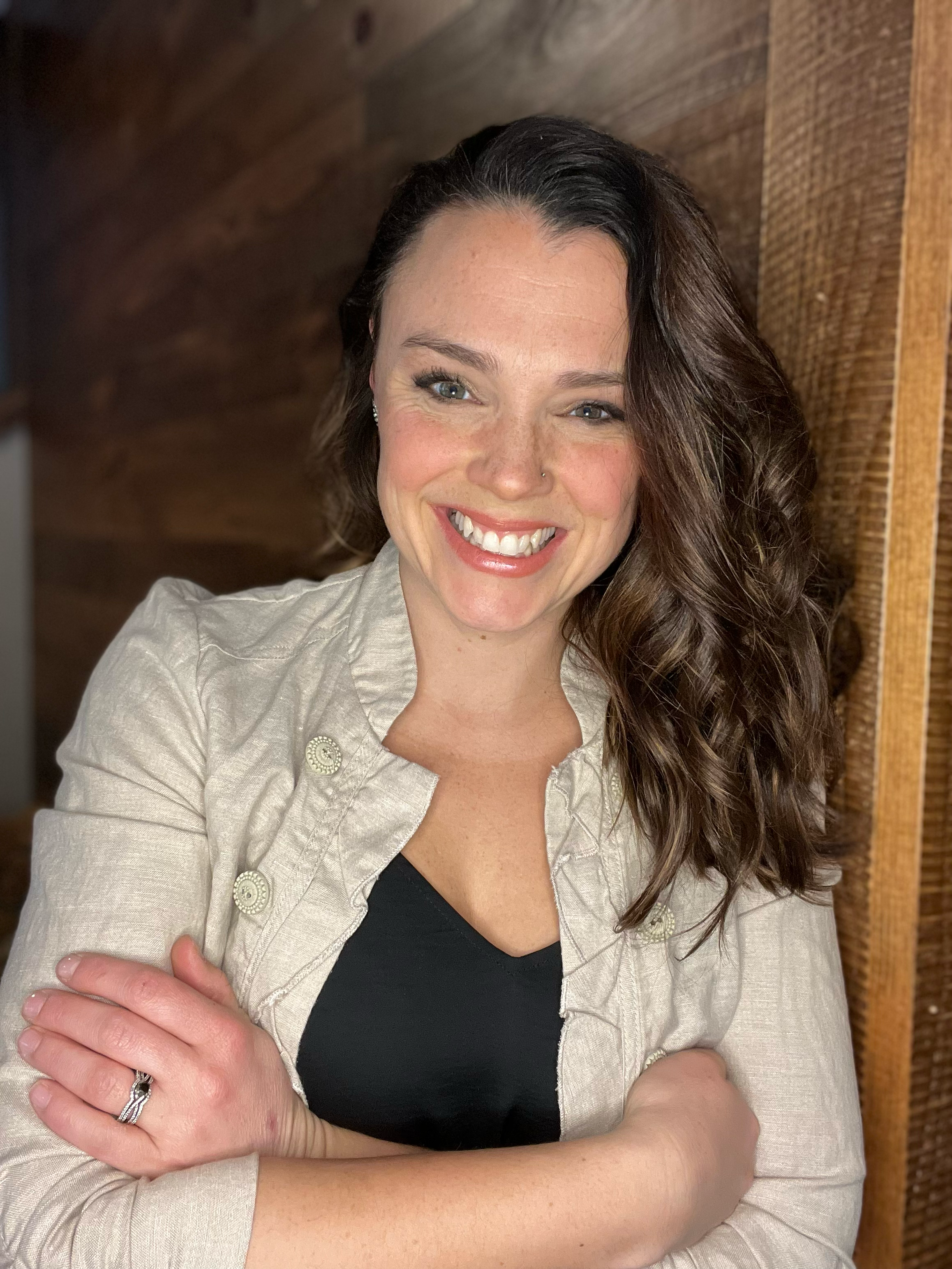 Kelly, smiling while posing with her arms crossed in front of her.