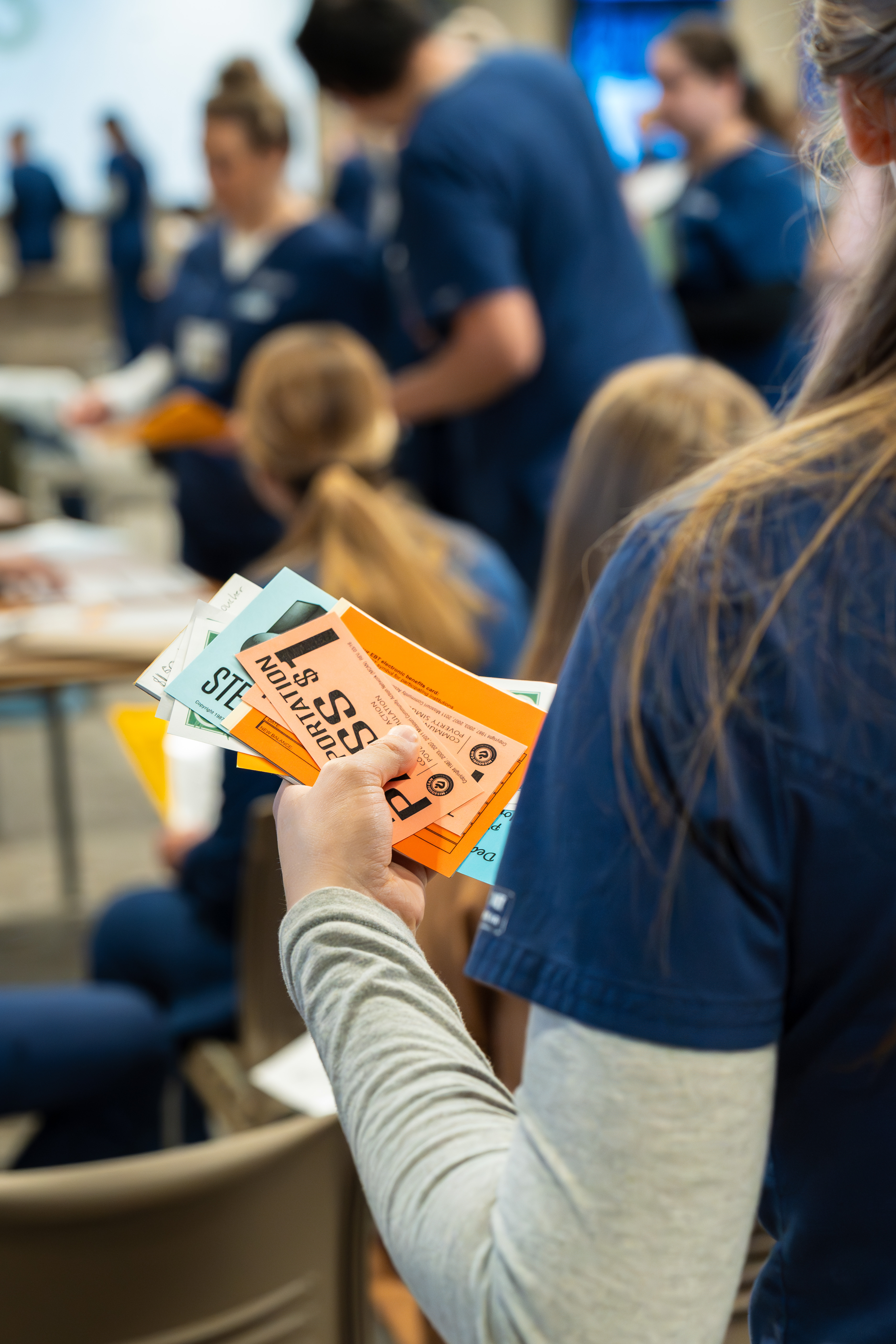 A Nursing student holding assorted papers and vouchers during a poverty simulation