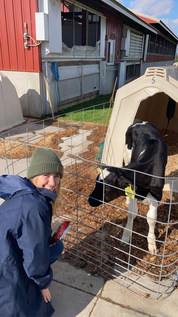 Savana Mata smiling while crouching next to a calf at the NTC Agriculture Center of Excellence.