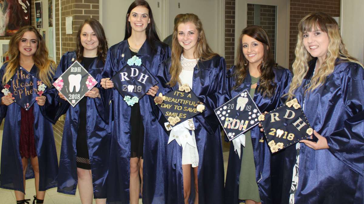 Six graduating students stand together holding their graduation hats