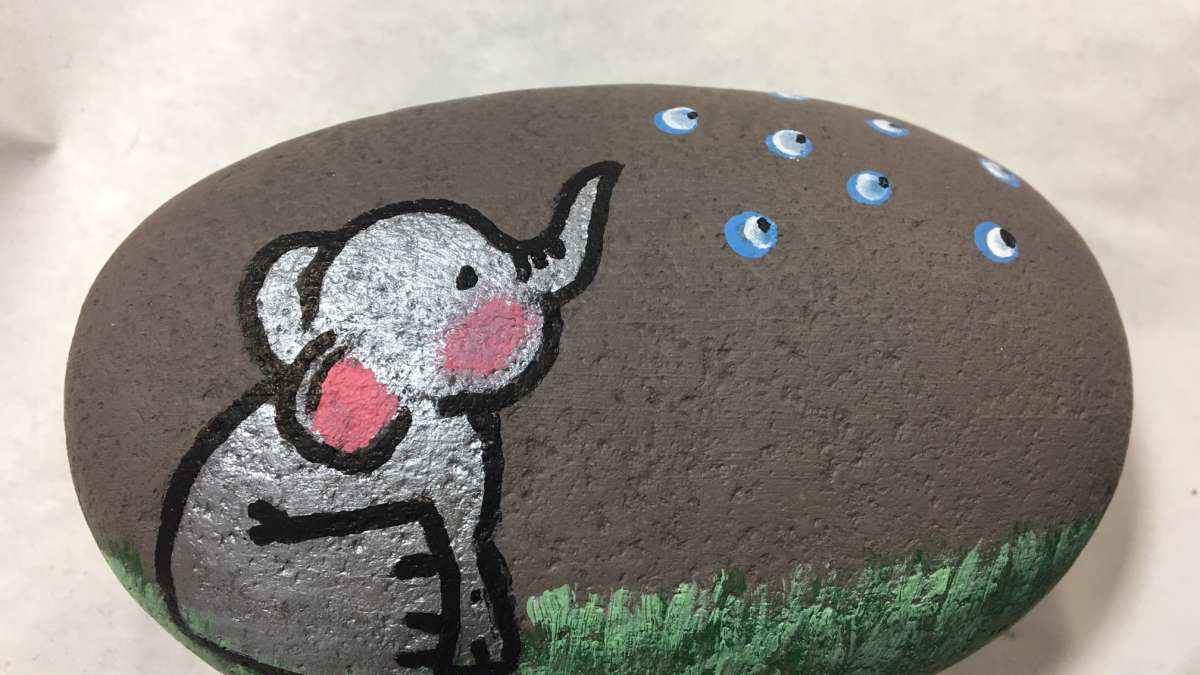 A rock painted with an elephant sitting on grass.