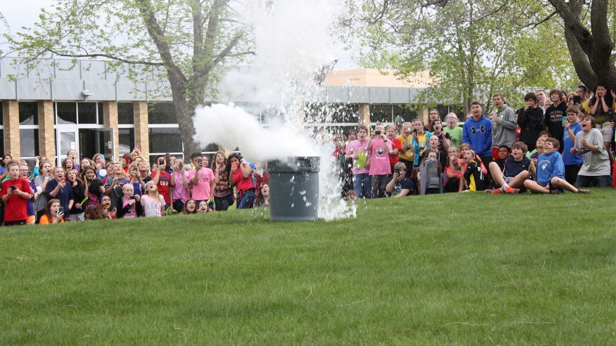 Students are gathered around a science experiment outside on the grass in NTC's Courtyard