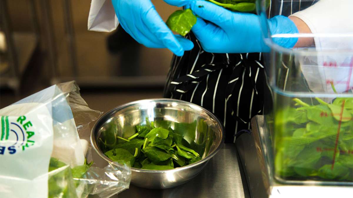 A chef is preparing spinach in an aluminum bowl
