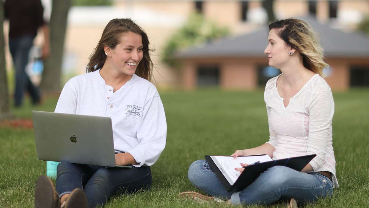 Two students are sitting on the grass having a conversation in the NTC Courtyard