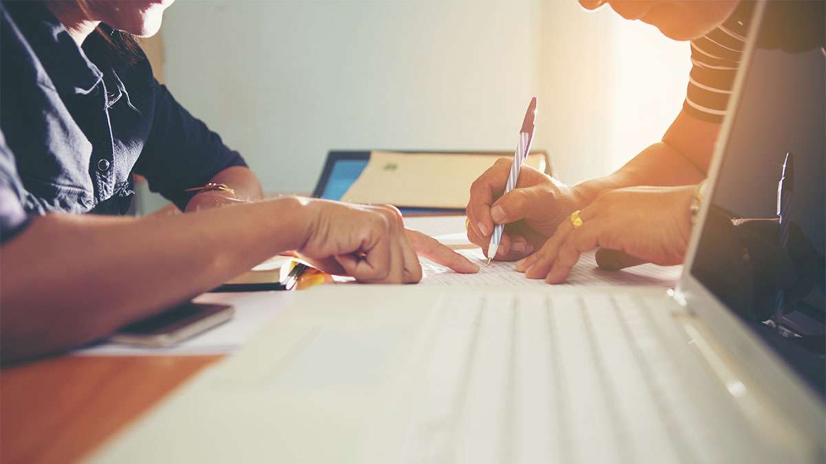 A man is sitting down at a table with another person writing down his information on a registration form