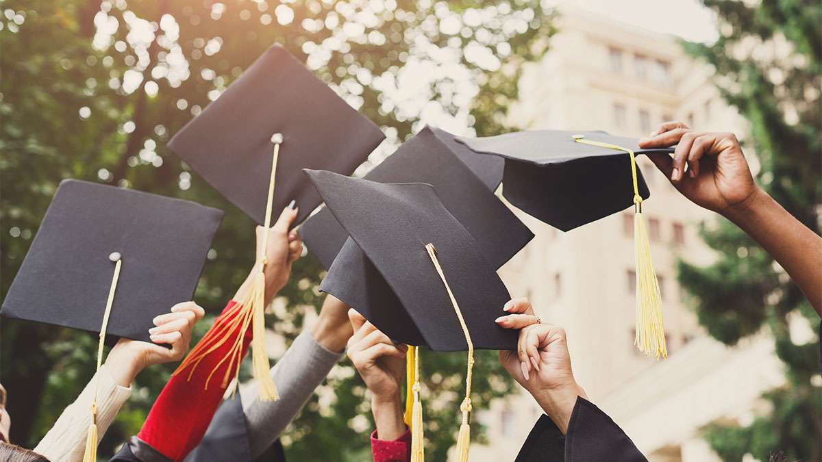 Several students are holding up their graduation hats