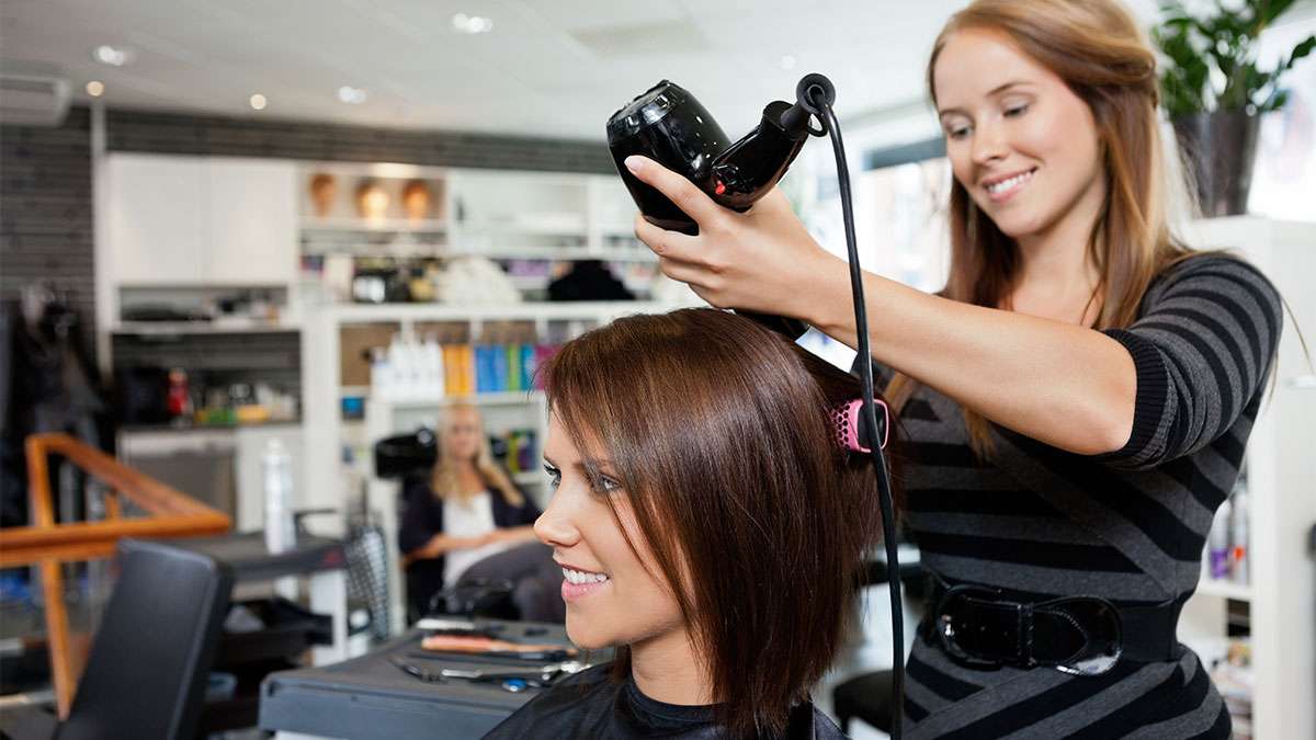 A hair stylist is using a hair dryer on a person who's hair she is styling