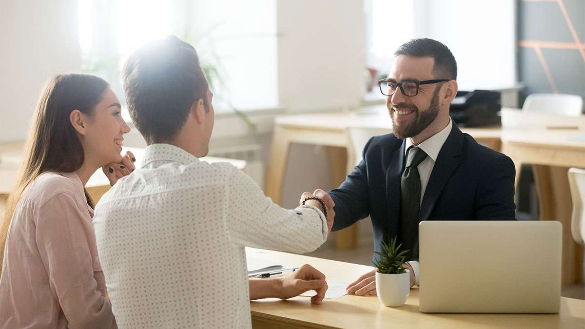 A couple sits in front of a financial advisor and shakes his hand