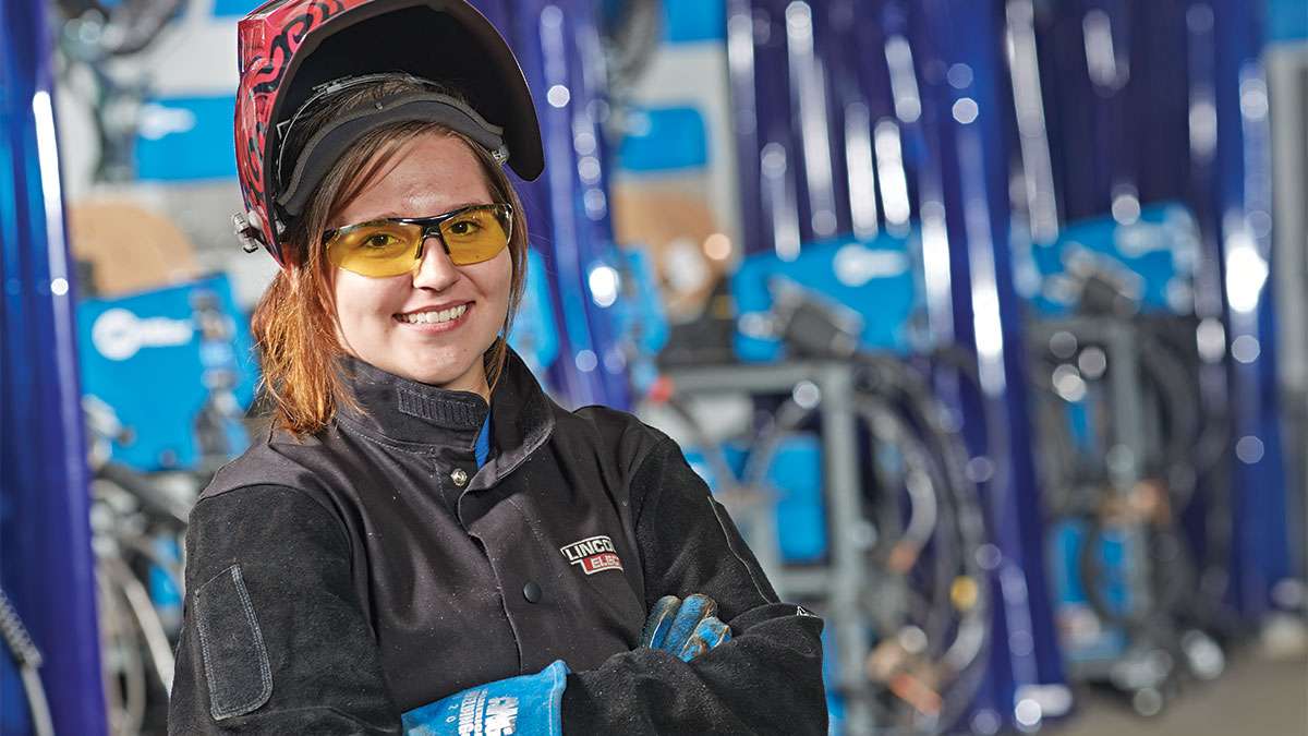 A student apprentice standing with her arms crossed in front of mechical equipment