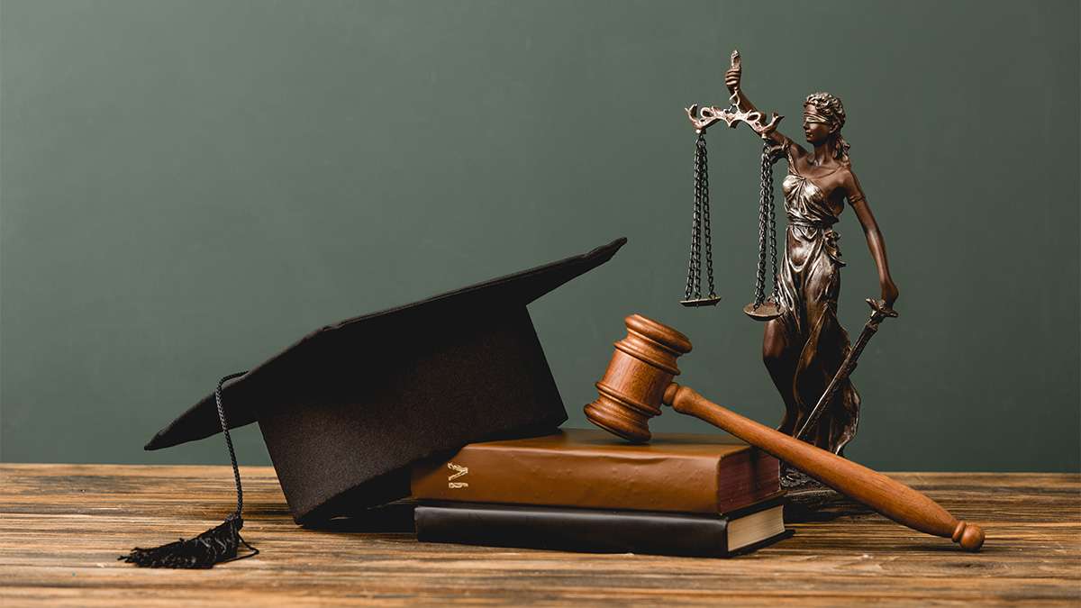 A graduation hat sits on top of a law book next to a gavel and lady justice