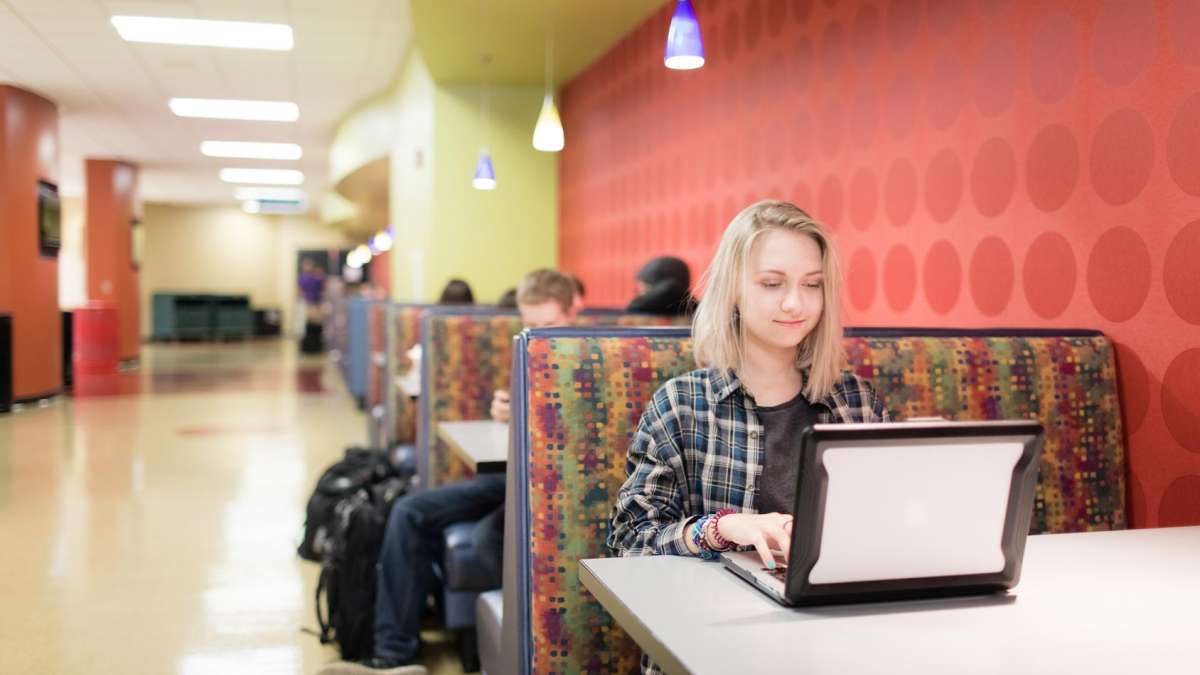 Student sitting at booth while typing on laptop