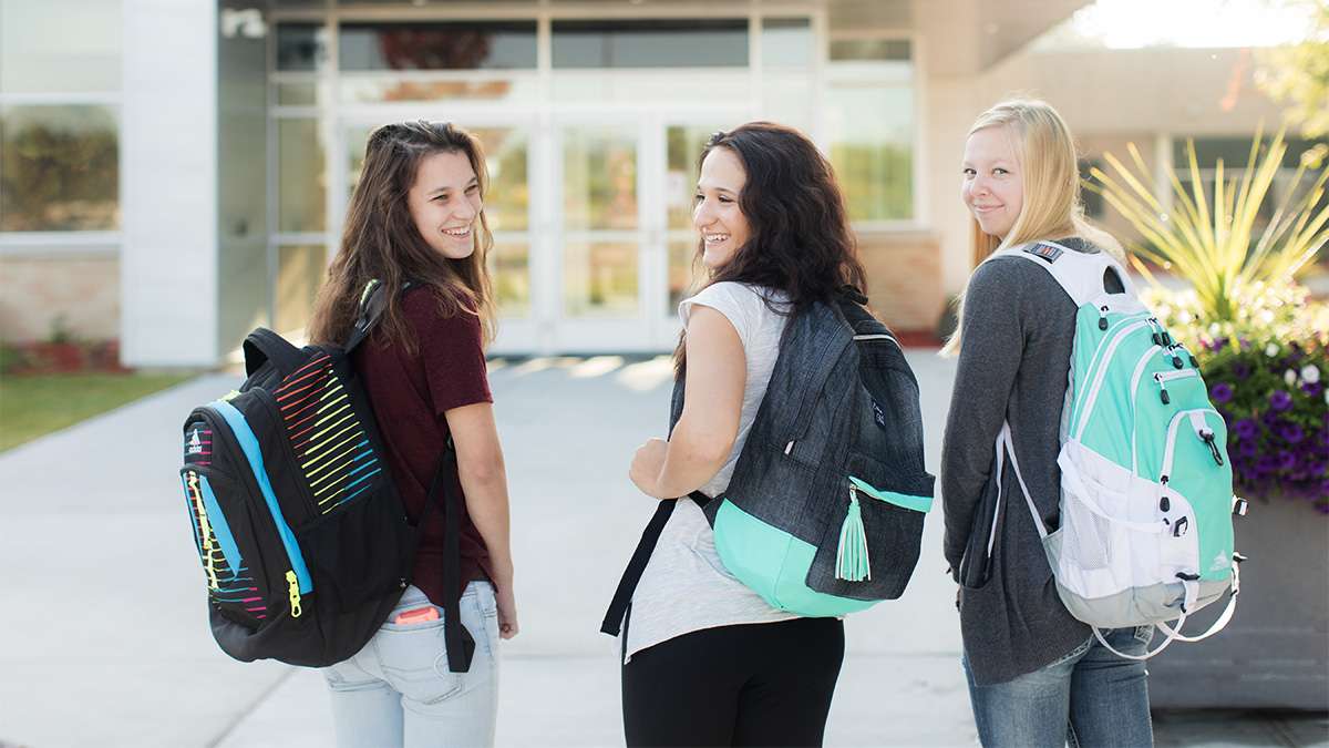 Three students wearing backpacks are walking towards the front entrance of Northcentral Technical College