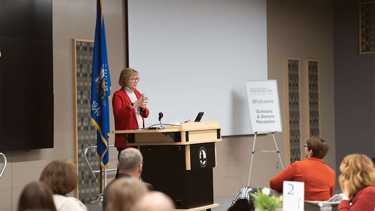 Dr. Lori Weyers stands in front of a podium giving a speech in front of an audience at Northcentral Technical College.