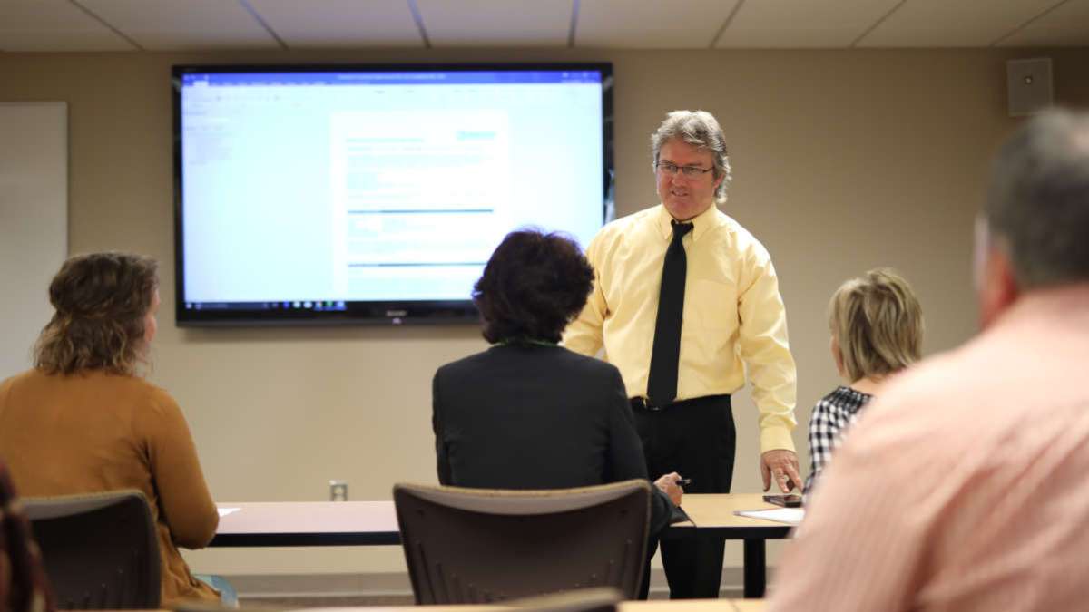 Instructor at front of classroom with students in chairs in front of him