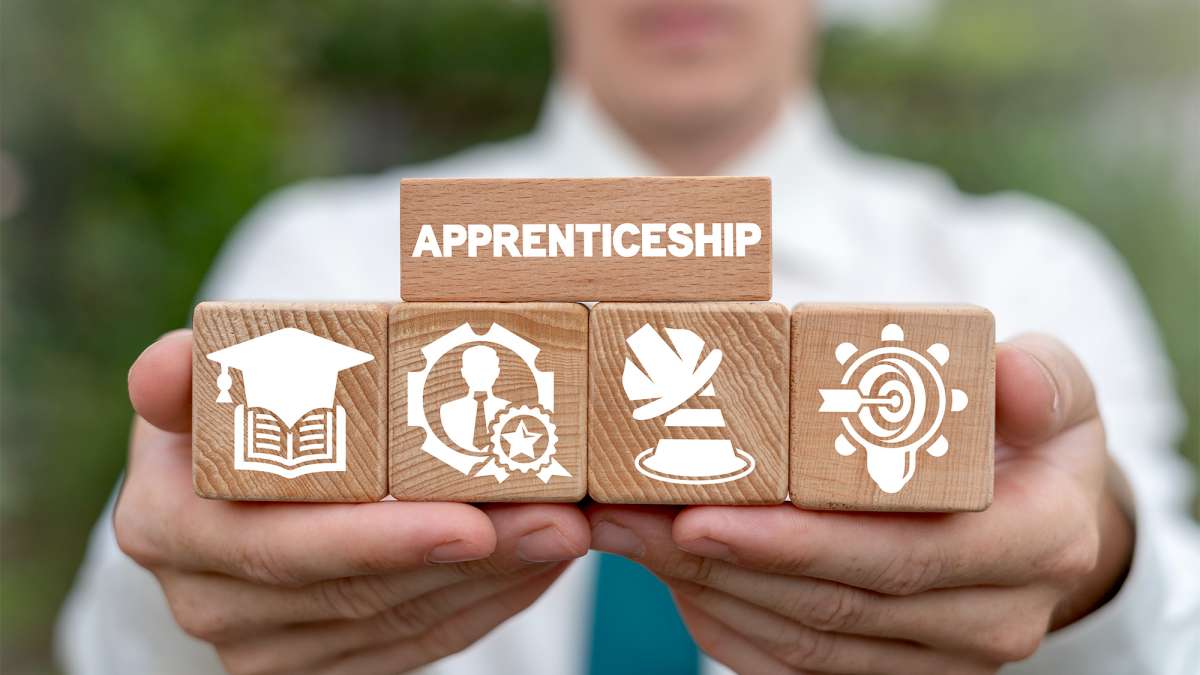 A man wearing a white shirt and blue tie is holding blocks with icons and one large block that says apprenticeship.