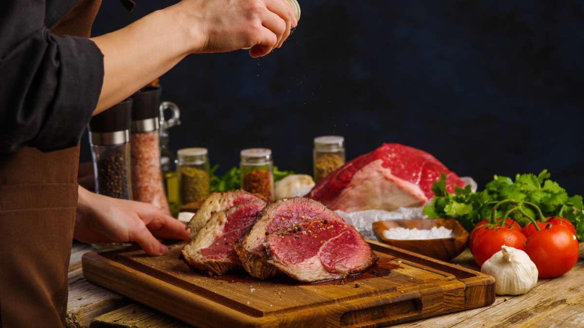 The chef sprinkles spices and seasonings on raw cuts of meat.