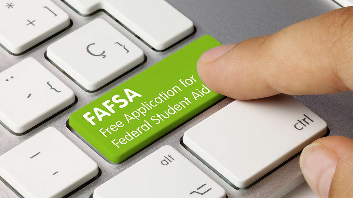 A finger presses down on a keyboard key that says "FAFSA free application for federal student aid".