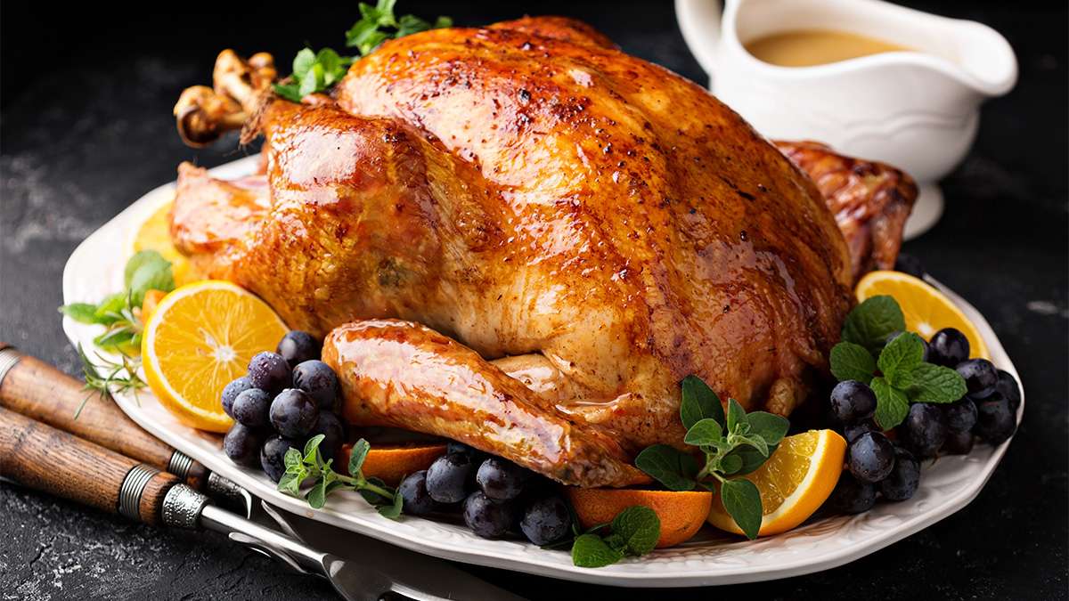 A roasted turkey on a plate surrounded by gravy and fruits.