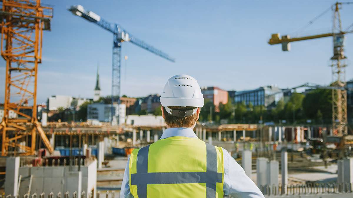 A civil engineer wearing safety gear looks over a construction site full of workers and construction equipment.