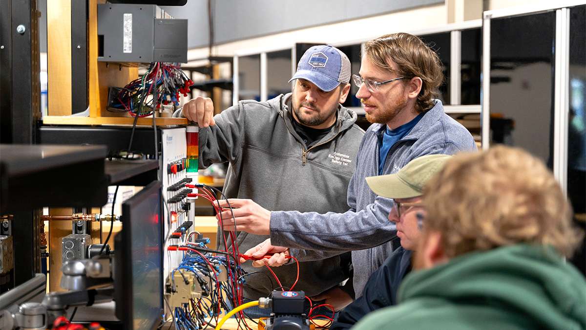 Three apprentices are being instructed as they work on electrical equipment.