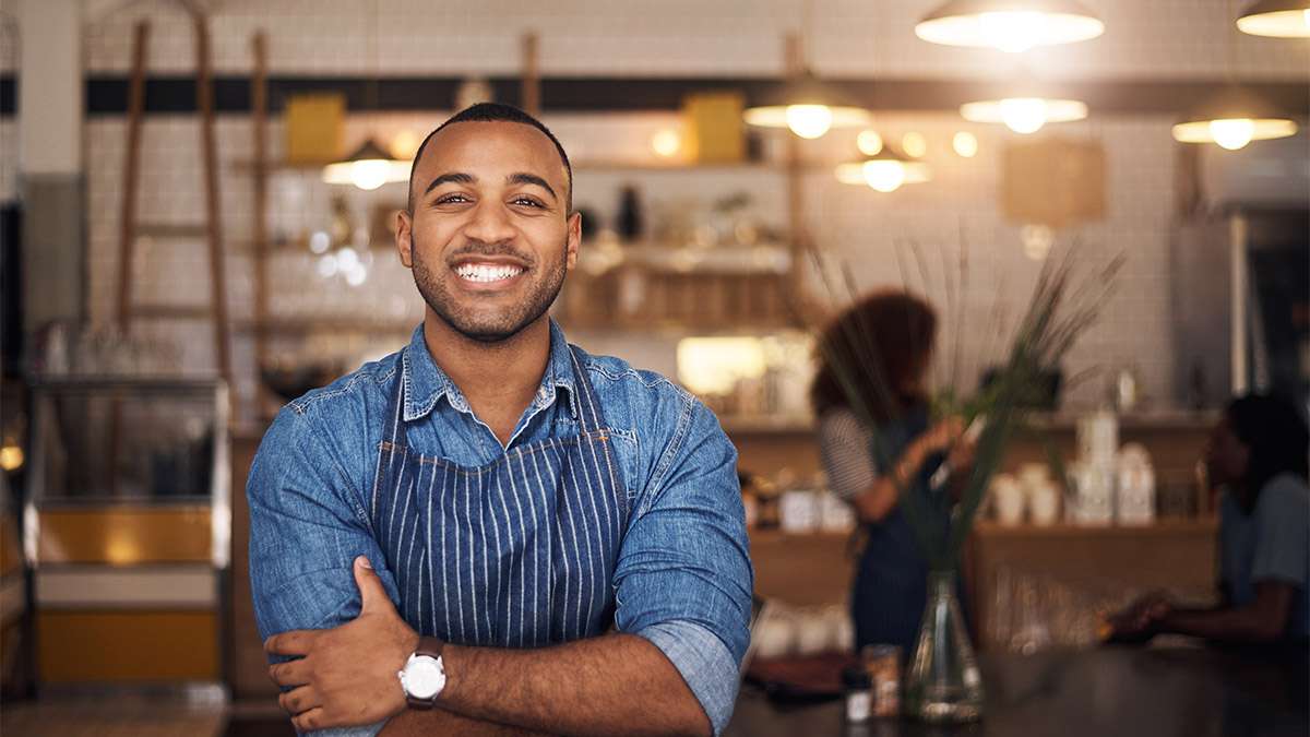 A Hospitality Manager smiles proudly with his arms crossed inside of his restaurant.