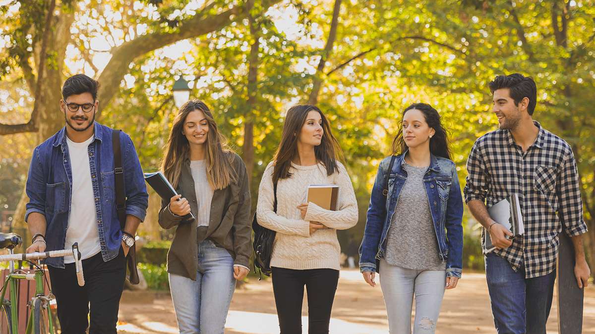 Five students walk together holding books and notepads in hand.