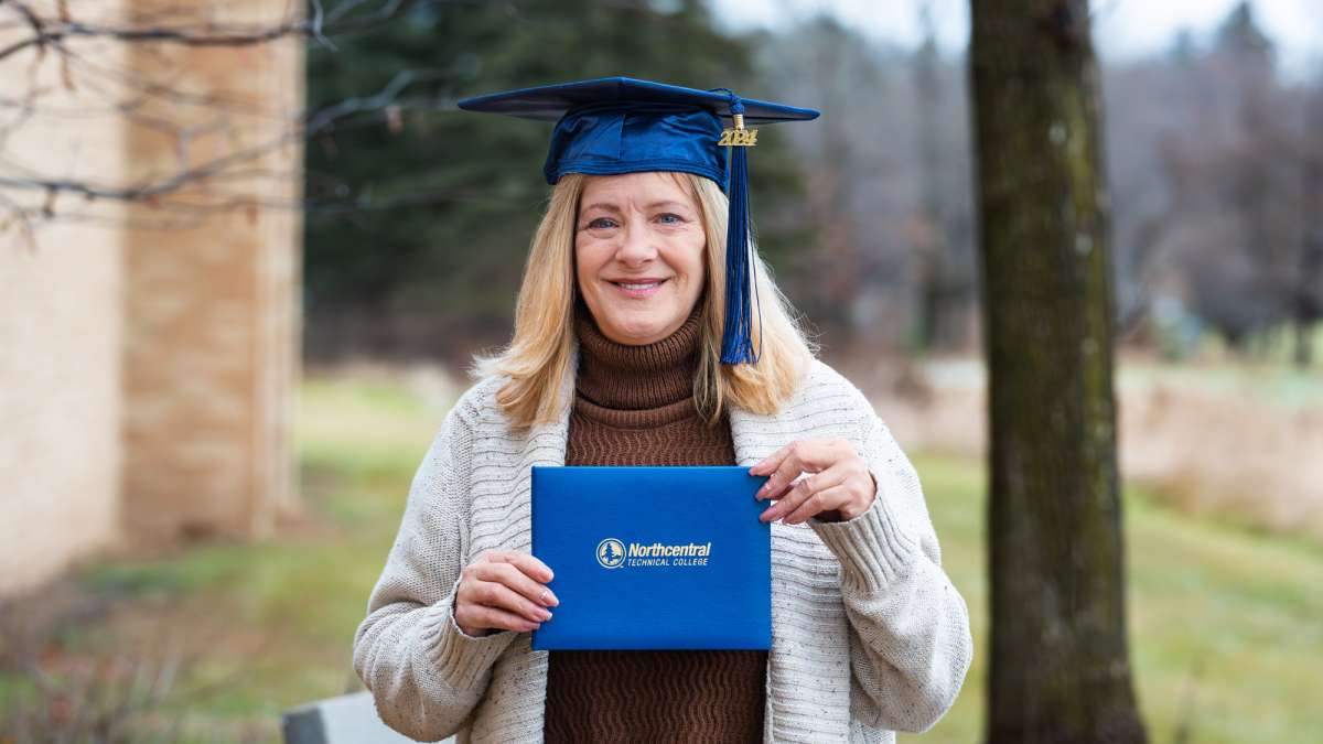 Jennifer posing while wearing an NTC graduation cap and holding her diploma.