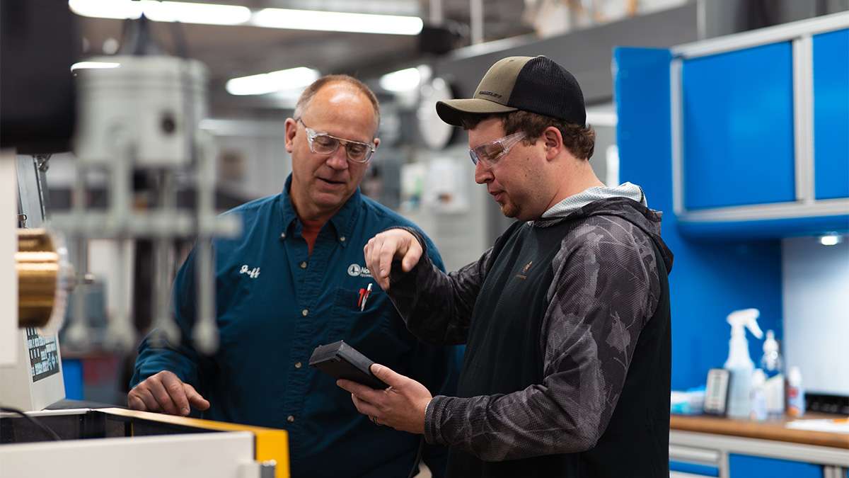 Two manufacturing workers collaborate, examining a component in a high-tech industrial workshop setting.