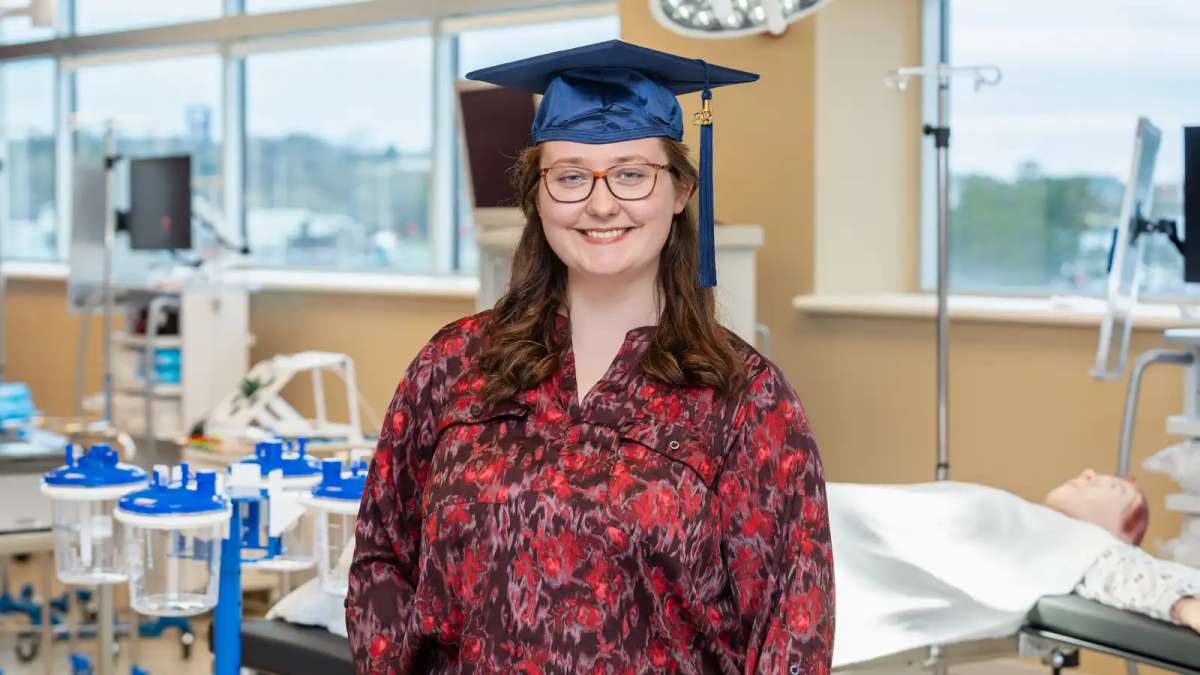 Adriana smiling while wearing her graduation cap while standing inside a lab in the Center for Health Science