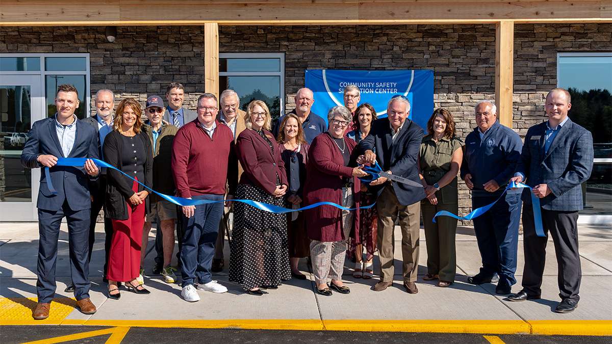 A large group of smiling people participates in a ribbon-cutting ceremony.